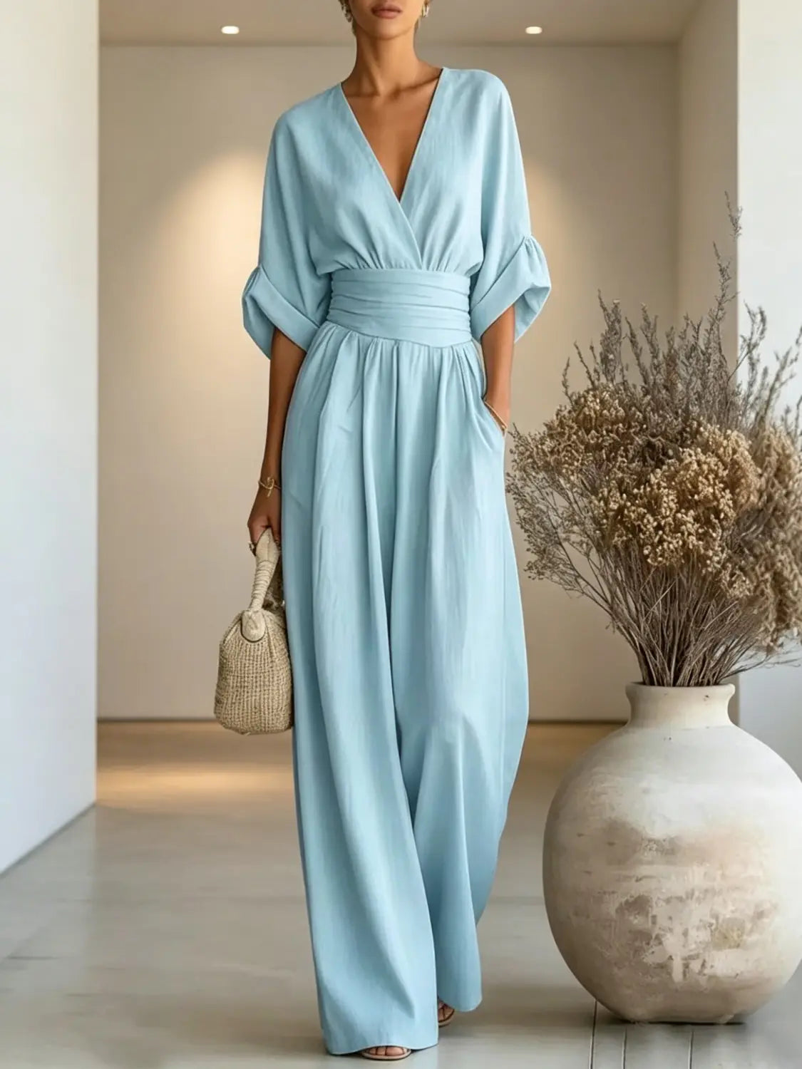 A flowing light blue wide-leg jumpsuit with a v-neckline, cinched waistband, and three-quarter length sleeves.