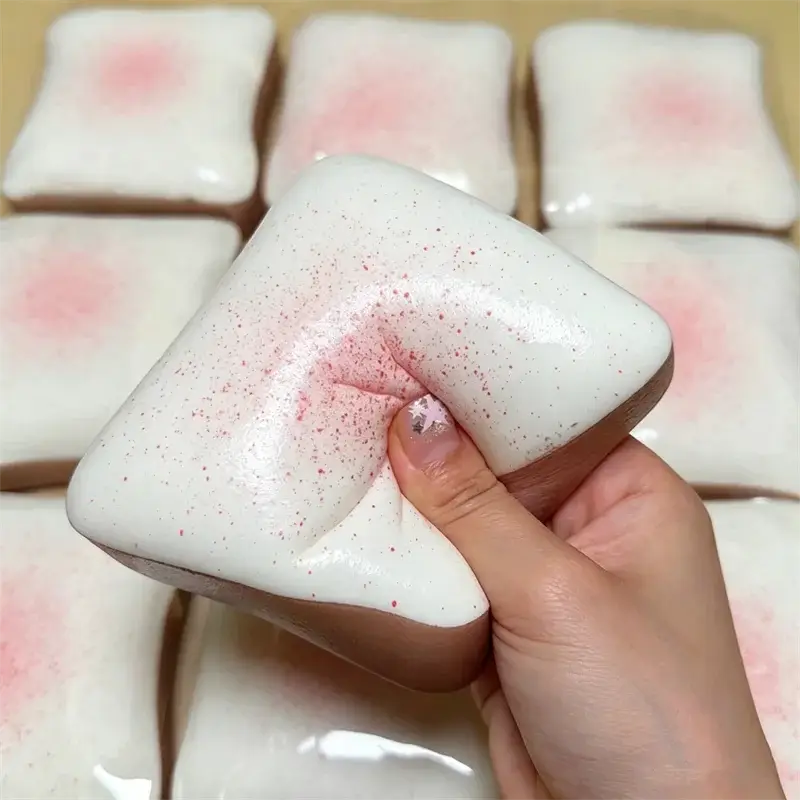 Jouet anti-stress en forme de toast moelleux blanc, à texture souple et légèrement extensible, avec des touches rose poudré, couleur macaron.
