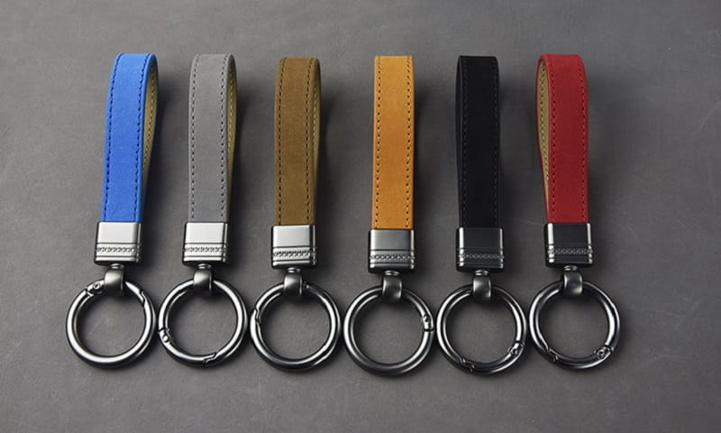 Six leather keychains set in blue gray tan yellow black and red each featuring a silver-toned metal clasp and ring.