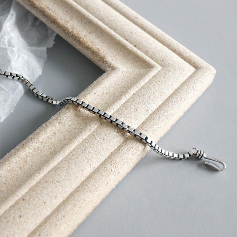 L’image présente un bracelet de charme en métal géométrique ton argent pour couples, doté d’une chaîne à boîte polie élégante et d’une fermeture sécurisée.