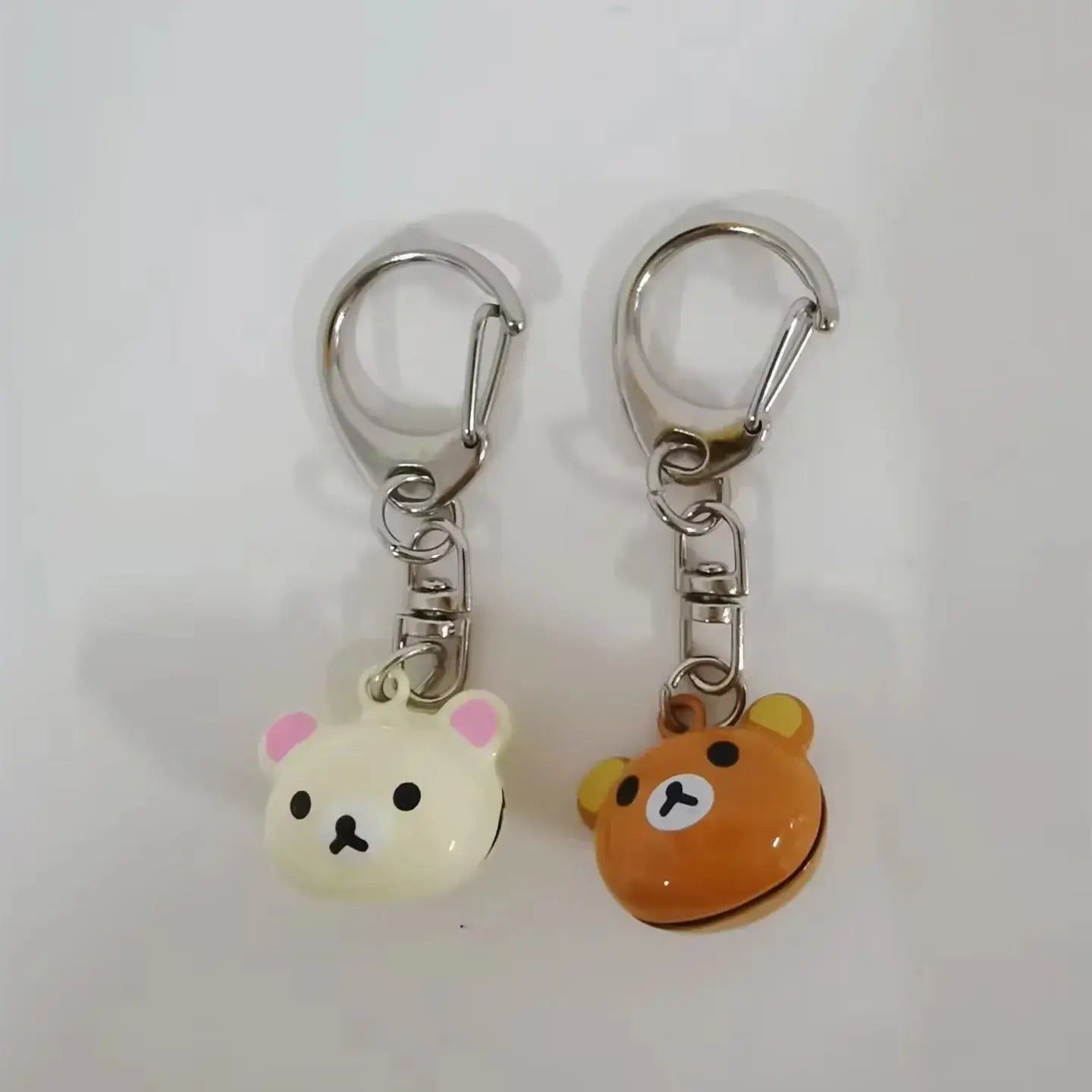 Two rilakkuma bear keychains featuring cream-colored and orange glossy plastic bears with metal clasps are cute enamel charms perfect for accessories.