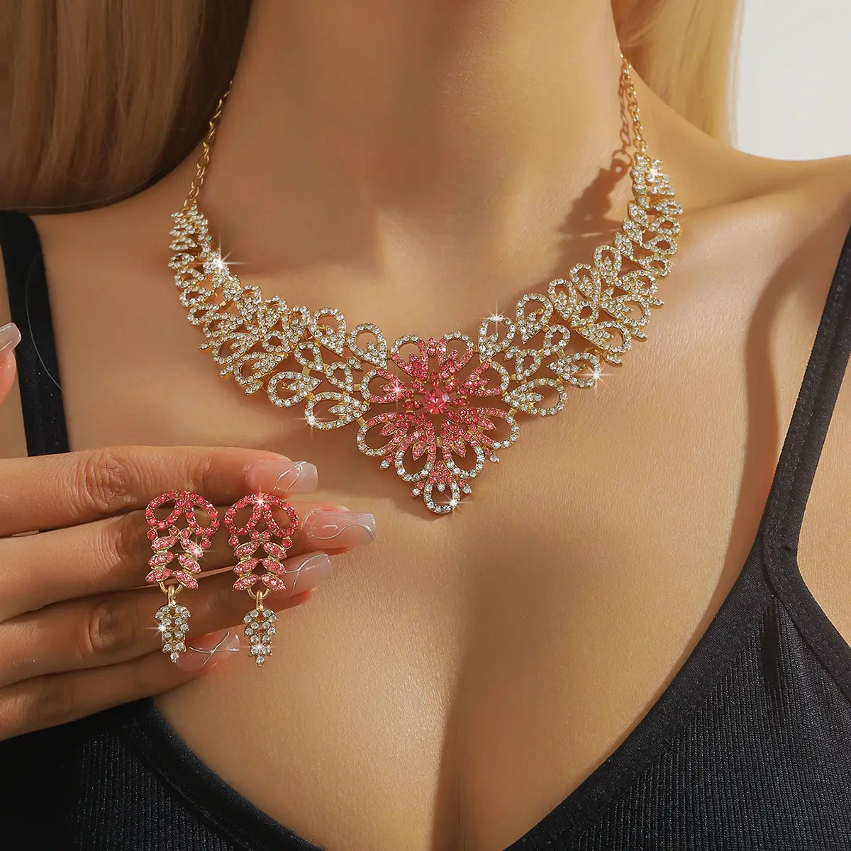 Un ensemble de bijoux en forme de fleur en cristal rose plaqué or, étincelant, comprenant un collier aux motifs floraux complexes et des boucles d’oreilles pendantes assorties.