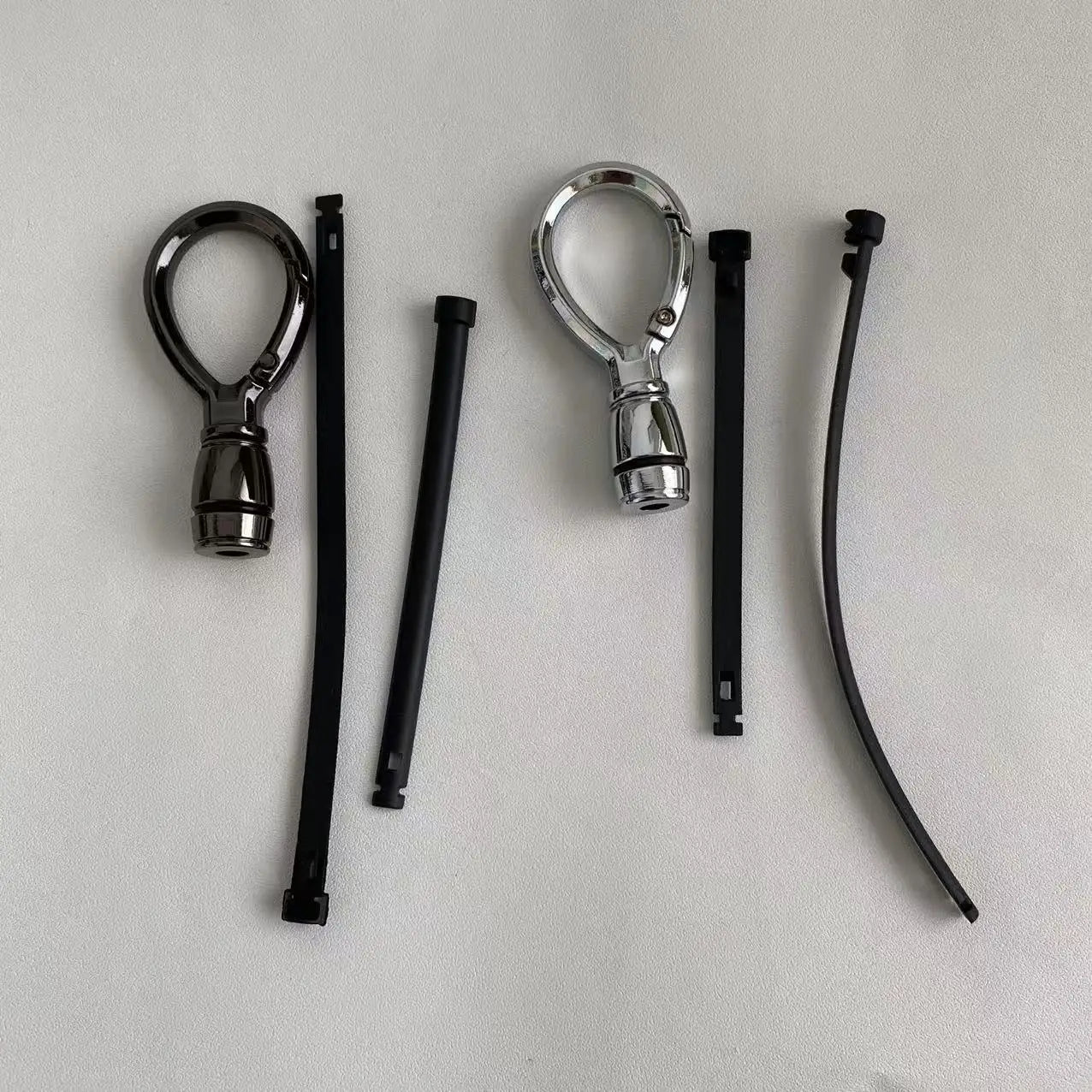 Dos accesorios de mosquetón magnético de metal para llavero, en negro y plata, cada uno con una brida zip de plástico negro a juego, para uso como anillo de llaves anti-pérdida.