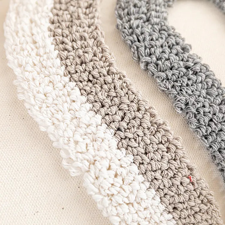 Handgehäkeltes Band mit einem weichen, strukturierten Muster aus abwechselndem Creme- und gedämpftem grauem Garn auf einem Kissenbezug 45x45 cm, Boho-Tufting grau, für die Heimdekoration.