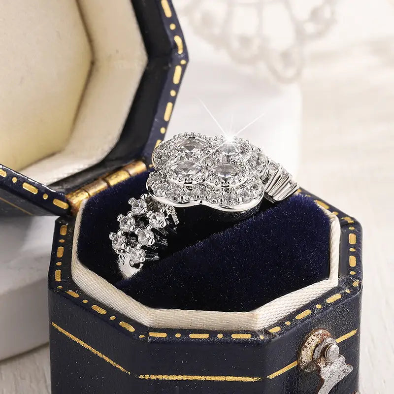 Un anillo de diamante de trébol de cuatro hojas de plata con brillo, con un conjunto de gemas facetadas transparentes en un diseño floral intrincado.