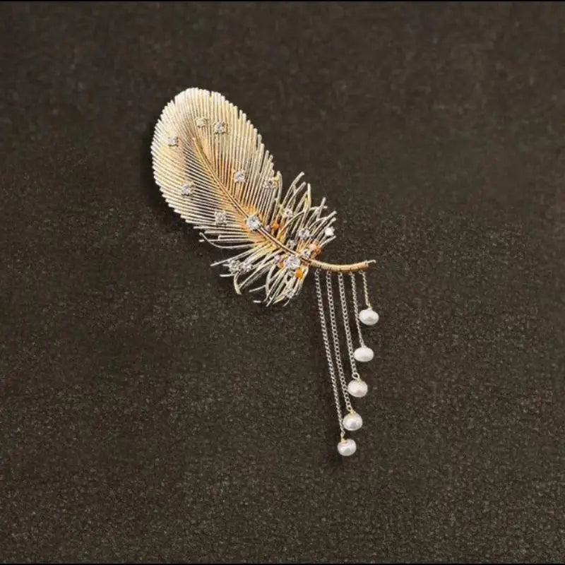 Broche à pompon en perles de plume dorée délicate, ornée de cristaux transparents étincelants et de perles blanches pendantes.