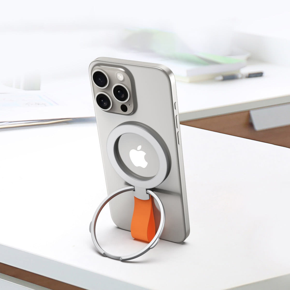 silver iphone backside featuring a magnetic phone ring holder with an orange silicone grip strap designed for magsafe compatibility