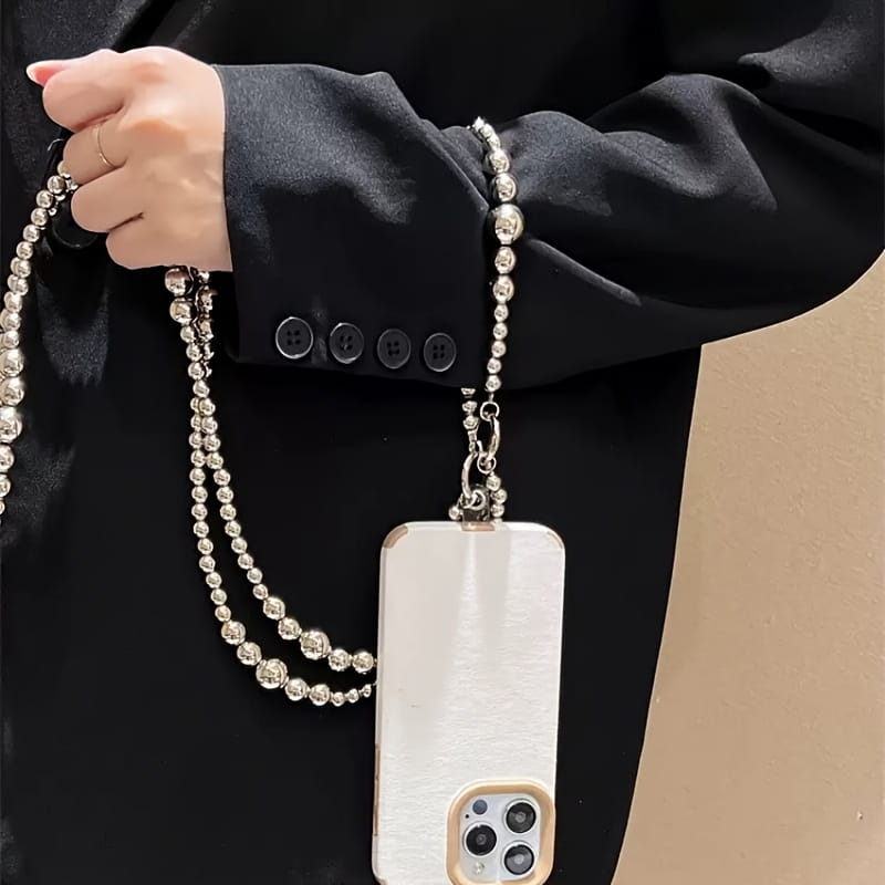 Funda para teléfono blanca y elegante con acabado metálico cepillado, sujeta a una correa decorativa para colgante de teléfono con cuentas plateadas y a una cadena de monedero.