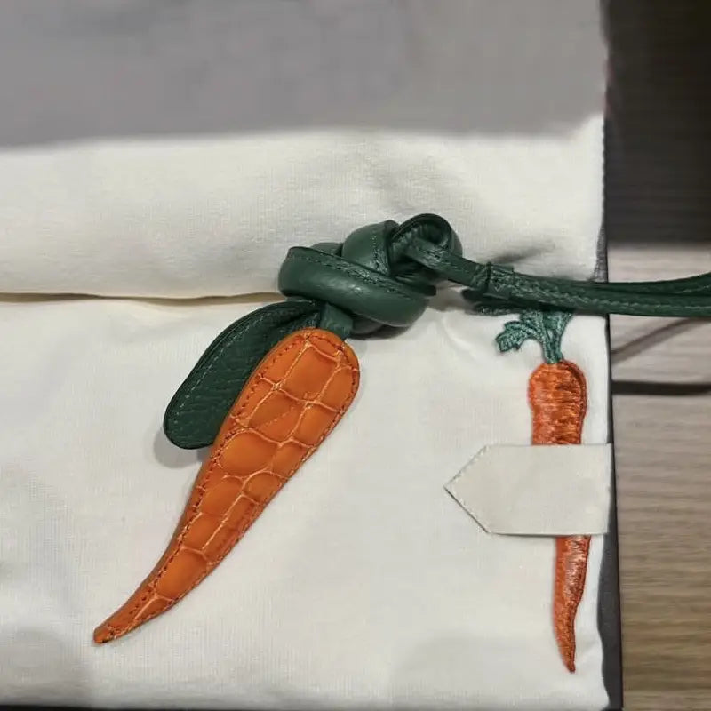 Un charm pour sac à main en cuir en forme de carotte, en crocodile orange, avec une tige en cuir vert et un nœud, pour ornement de sac à main de créateur.