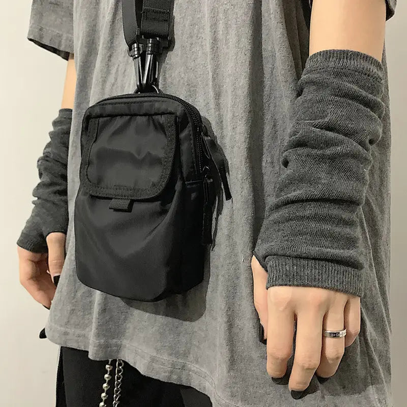 Black nylon crossbody bag with a front zippered pocket and adjustable strap shown with striped knit fingerless arm warmers.