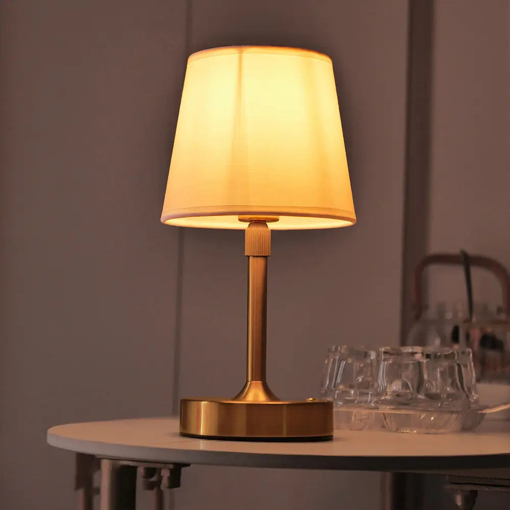 Warmtonige Messing-Touch-Tischlampe mit einem weichen cremefarbenen, plissierten Stoffschirm, von vorn dargestellt.