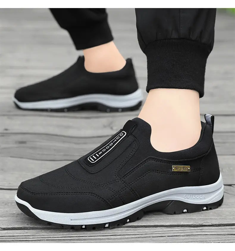 Men orthopedic slip-on walking shoe in black with a white midsole and black outsole featuring a textured rubber grip pattern.