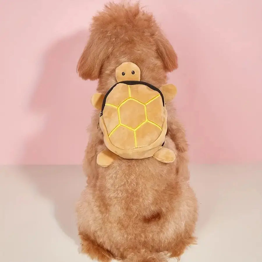 Una mochila de perro con forma de tortuga de felpa color beige suave, con detalles de costuras amarillas en patrones hexagonales en el caparazón y detalles de cremallera negra, diseñada para transportar mascotas.