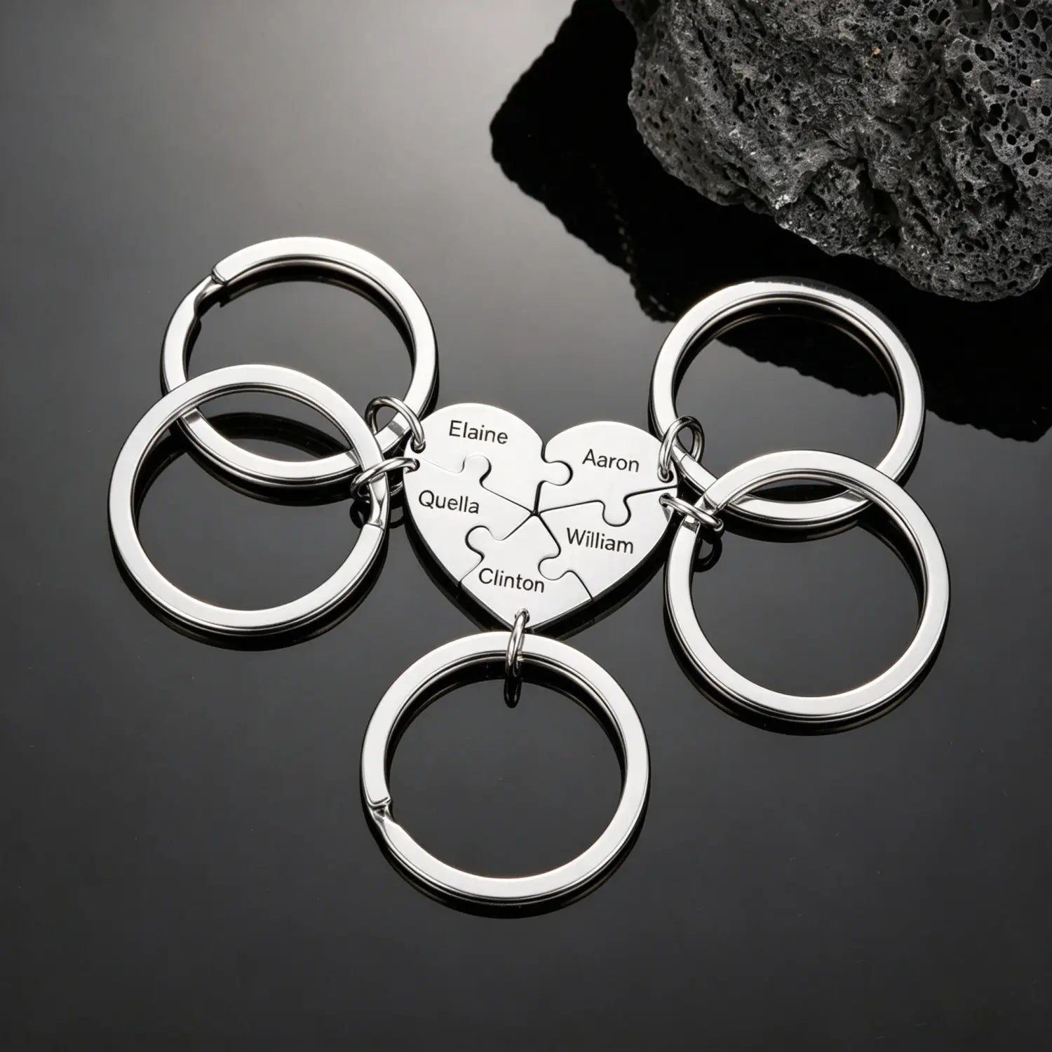 Silver heart-shaped keychain made of metal featuring a puzzle-piece design engraved with the names elaine, aaron, quella, william, and clinton in the custom family puzzle heart keychain collection.