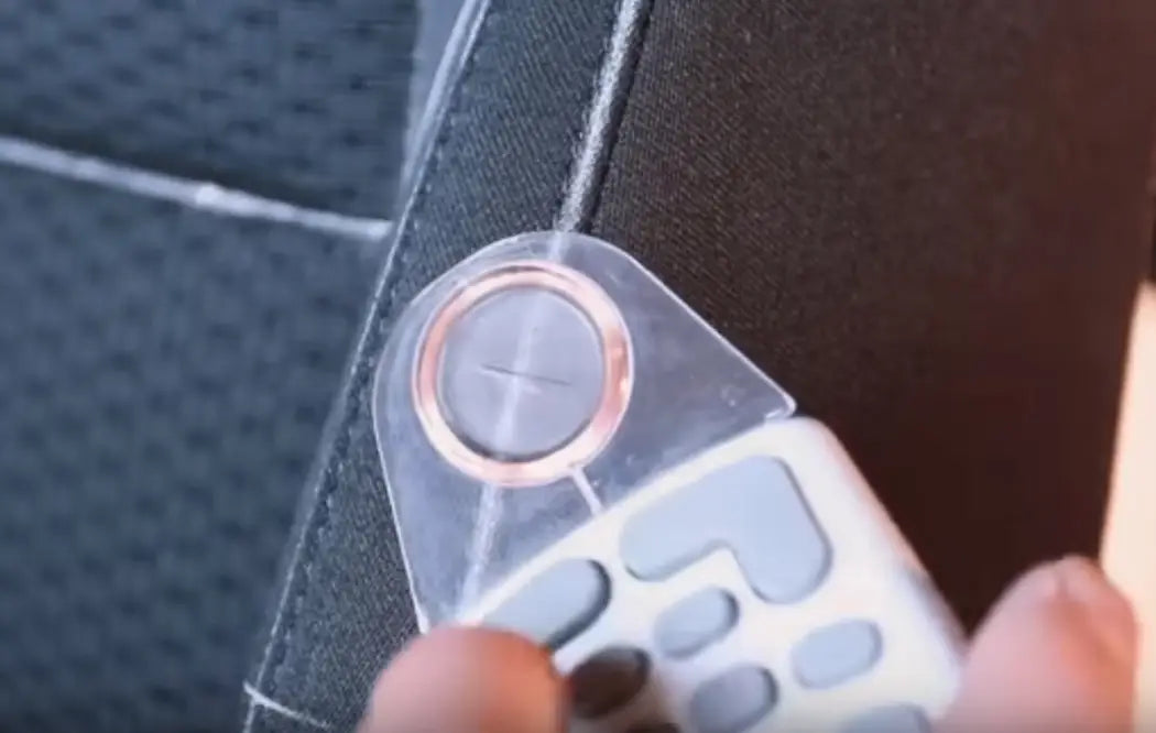 Una funda de control remoto de plástico transparente con botón circular color oro rosa y botones grises tipo teclado, diseñada para su uso con el juego completo de fundas universales para asiento de automóvil en negro y color canela