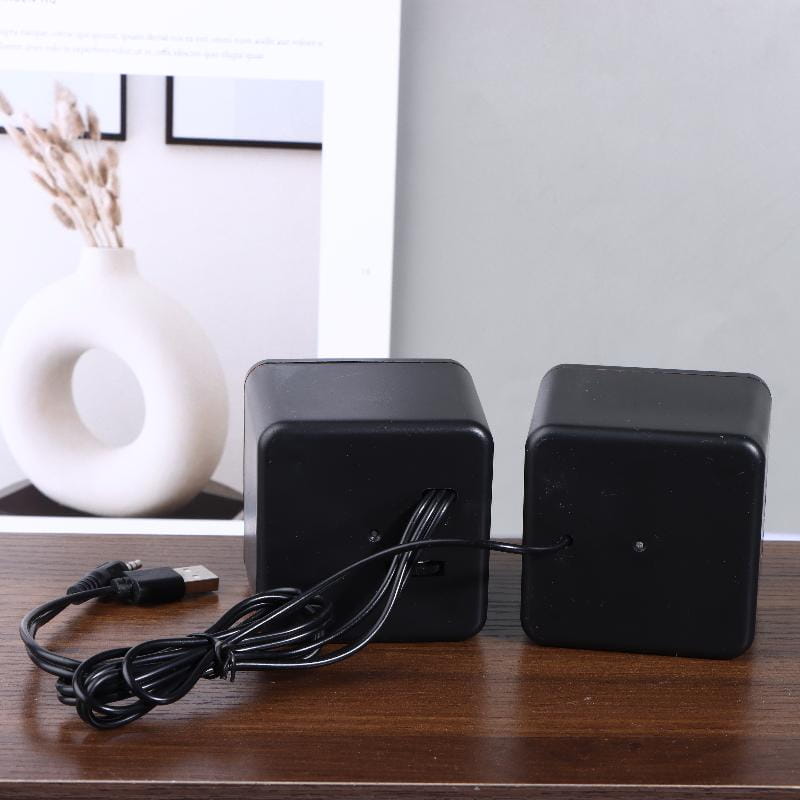 Black cube-shaped usb computer speakers with a matte finish connected by a coiled usb cable for led stereo desktop pc audio.