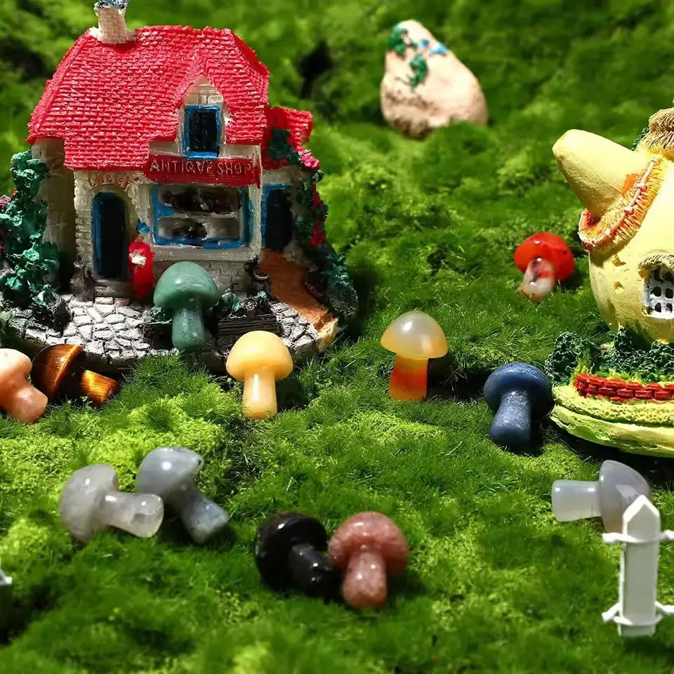 Una figurita miniatura de una antigua tienda con techo rojo, ventanas azules y un sendero de piedra, rodeada de coloridas figuras de hongos de resina sobre un musgo verde para la decoración natural de mini jardines con cristales.