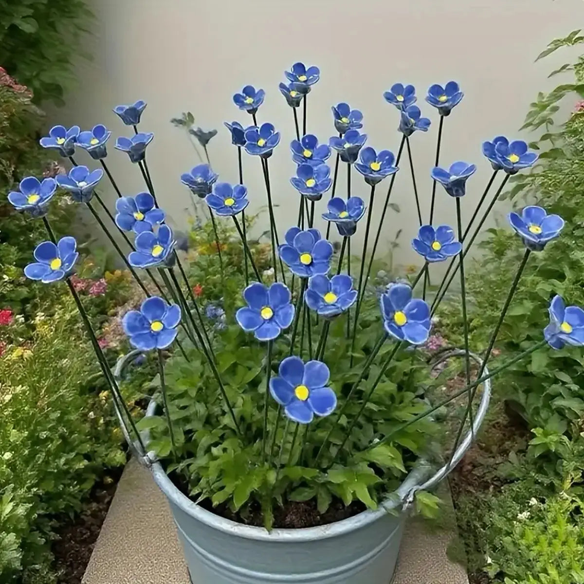 A cluster of vibrant blue ceramic artificial flowers with yellow centers arranged in a rustic galvanized bucket for decorating vases.