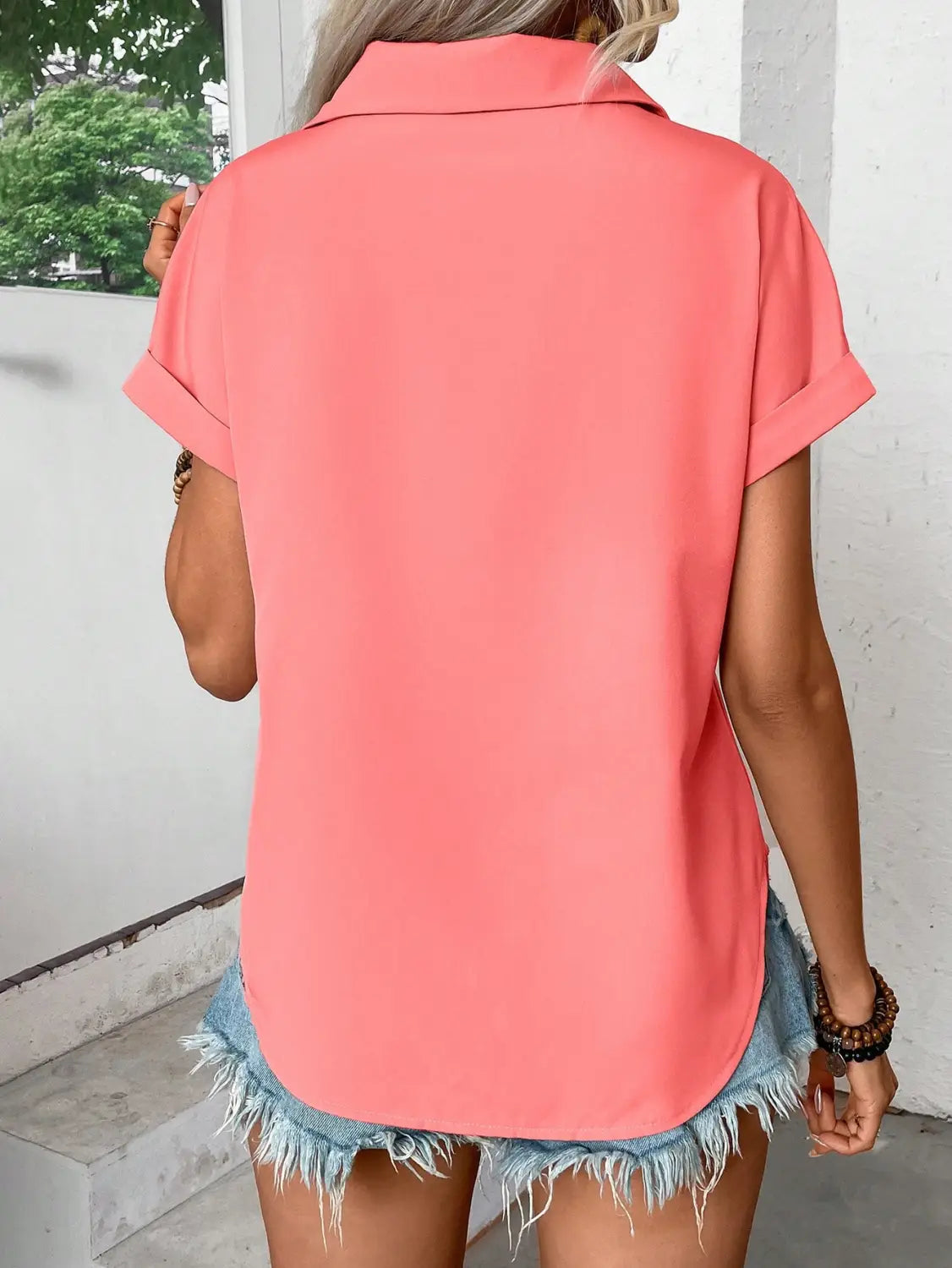 A soft coral-colored short sleeve button up blouse for women featuring a relaxed fit and rolled cuffs.