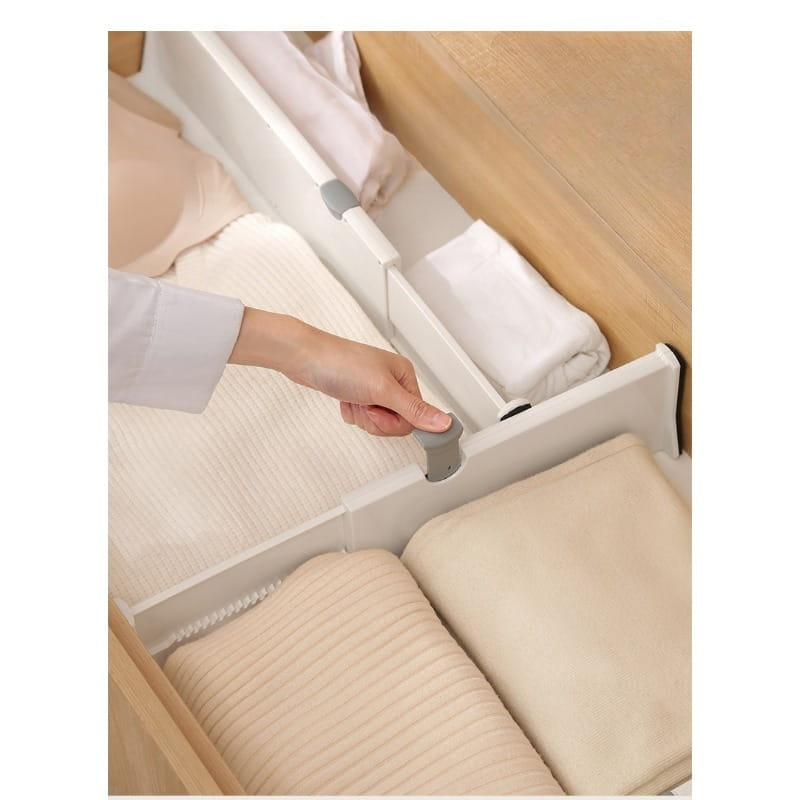 cloison de tiroir en plastique blanc avec poignées grises, séparant avec soin les linges beige pliés dans une commode en bois, pour une organisation de rangement ajustable.