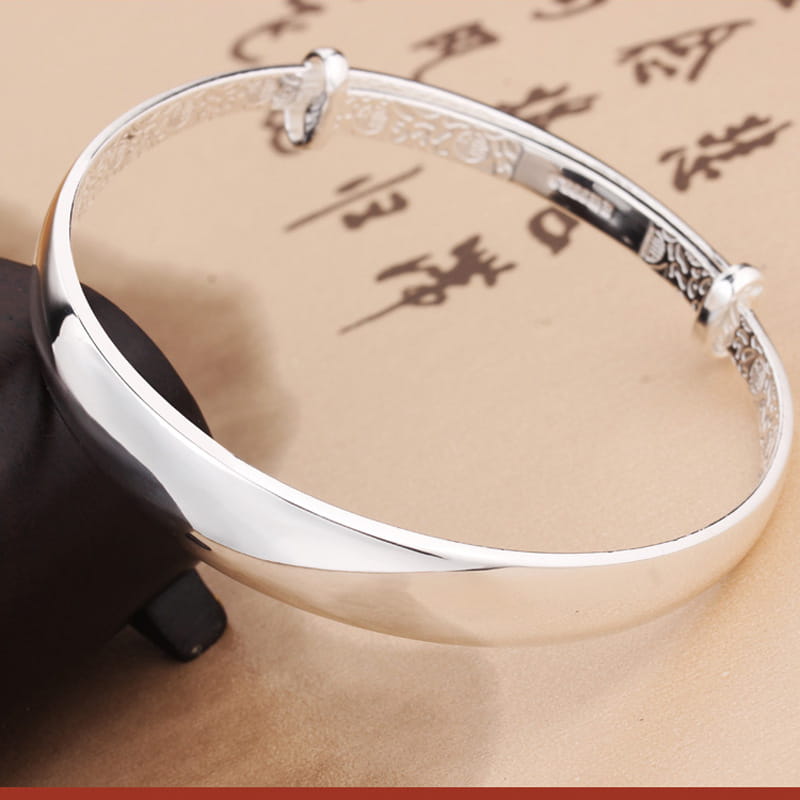 Sterling silver round bangle bracelet for women featuring an intricate engraved pattern and a polished reflective finish.