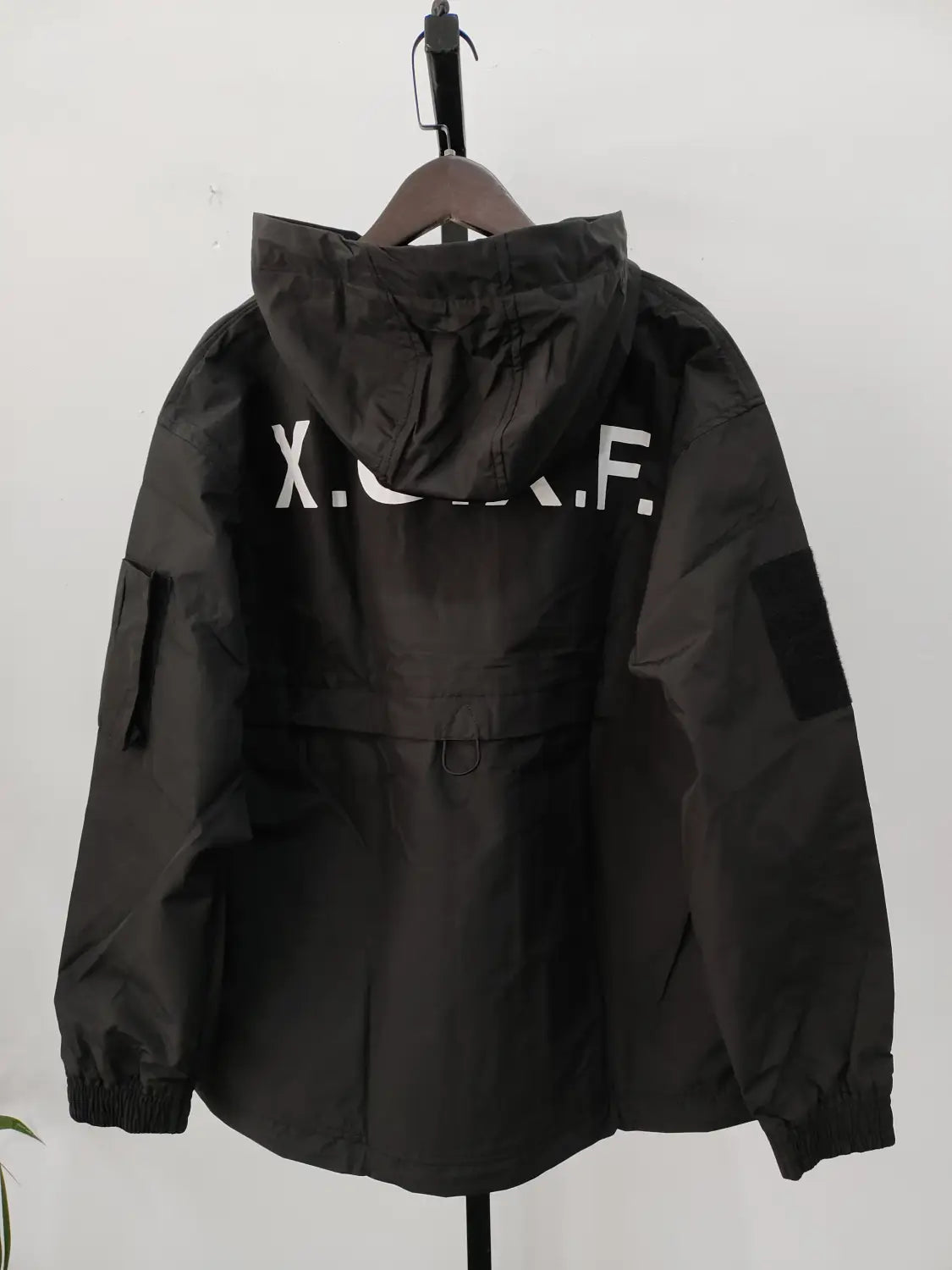 Veste imperméable à capuche tactique techwear noire x.c.f, présentée de dos, mettant en évidence sa matière imperméable durable, conçue pour un usage en extérieur