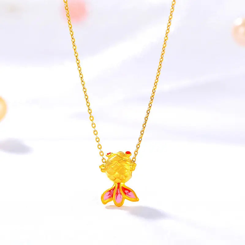 Collier pendentif poisson en or 24 carats, présentant des accents émaillés rouges au niveau des yeux et de la queue, suspendu à une délicate chaîne en or.
