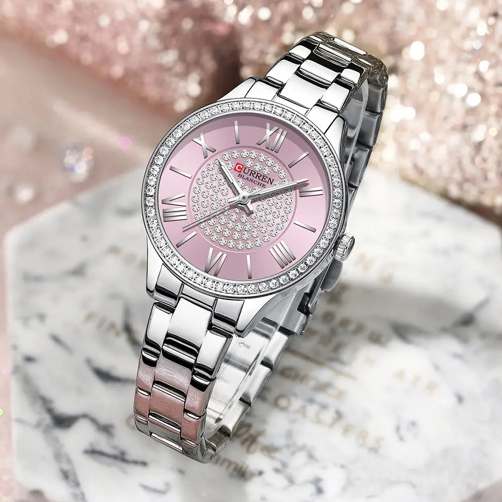 A Curren women stainless steel crystal quartz watch featuring a sleek silver-toned case with a pink dial adorned with sparkling crystals and roman numerals and an elegant stainless steel bracelet.