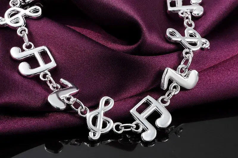 Silver musical note sterling silver bracelet featuring polished metallic links and intricate treble clef designs.