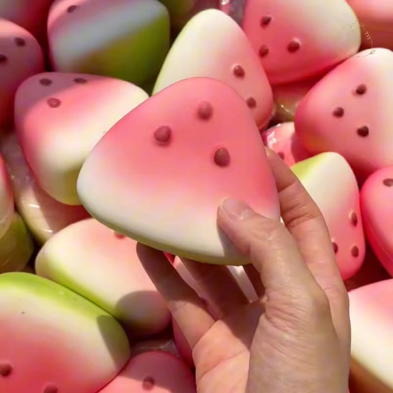 Une vue de face d’un jouet antistress « squishy » en forme de tranche de pastèque, avec un dégradé rose et vert, présentant des détails de graines rouges pour soulager le stress.