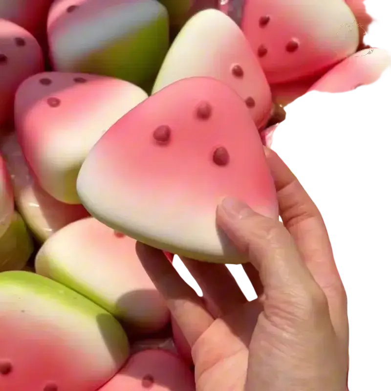 A hand holds a pink and white gradient watermelon-shaped slow rising squishy toy with red seed details front view