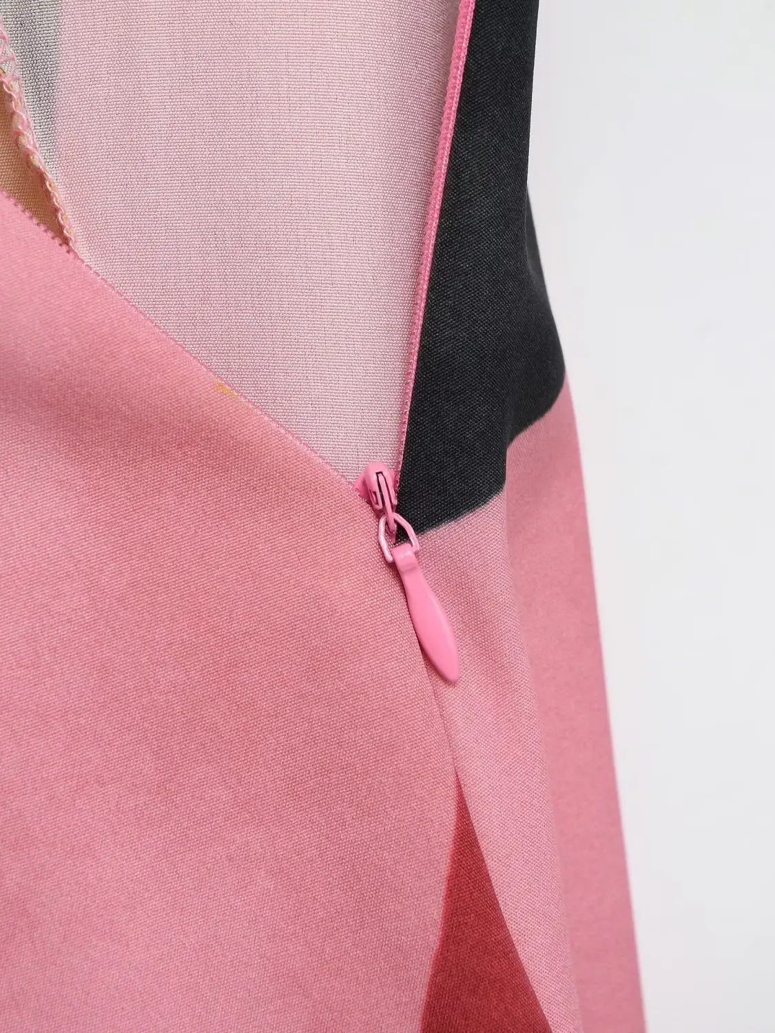 Ein geometrischer Satin-Midirock mit einem rosa Reißverschluss und einer eingenähten Reißverschlusslasche an der Seitennaht, mit kontrastierendem schwarzem und transparentem Mesh-Gewebe