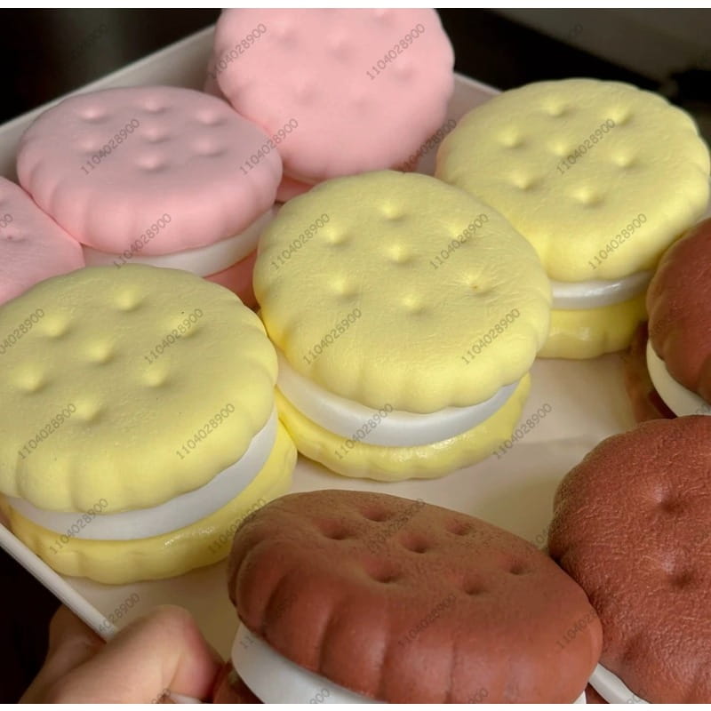Ein langsam ansteigendes großes Keks-Knautschspielzeug mit Pastellfarbenen, weich strukturierten Sandwich-Keksen, cremig-weißem Füllmaterial und einem realistischen Kuchen-Erscheinungsbild in Pink, Gelb und Braun.