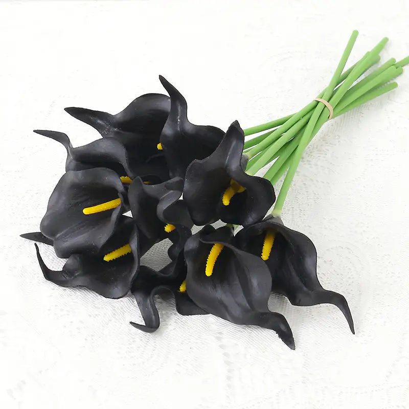 a bouquet of artificial black calla lilies with vibrant yellow spadices and green stems tied together for home decor.