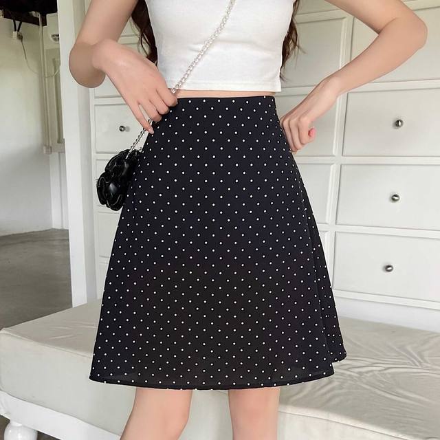 Falda midi línea A negra con lunares blancos y pretina ajustada mostrada desde el frente modelando un estilo de falda midi línea A roja con lunares.