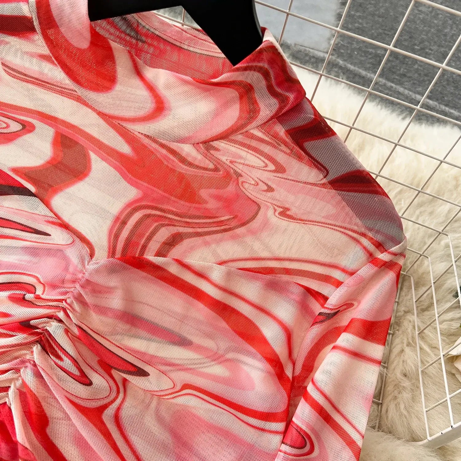 a flowing sheer two piece mesh skirt set with a vibrant red and pink marbled pattern and elastic closure hangs on a black hanger