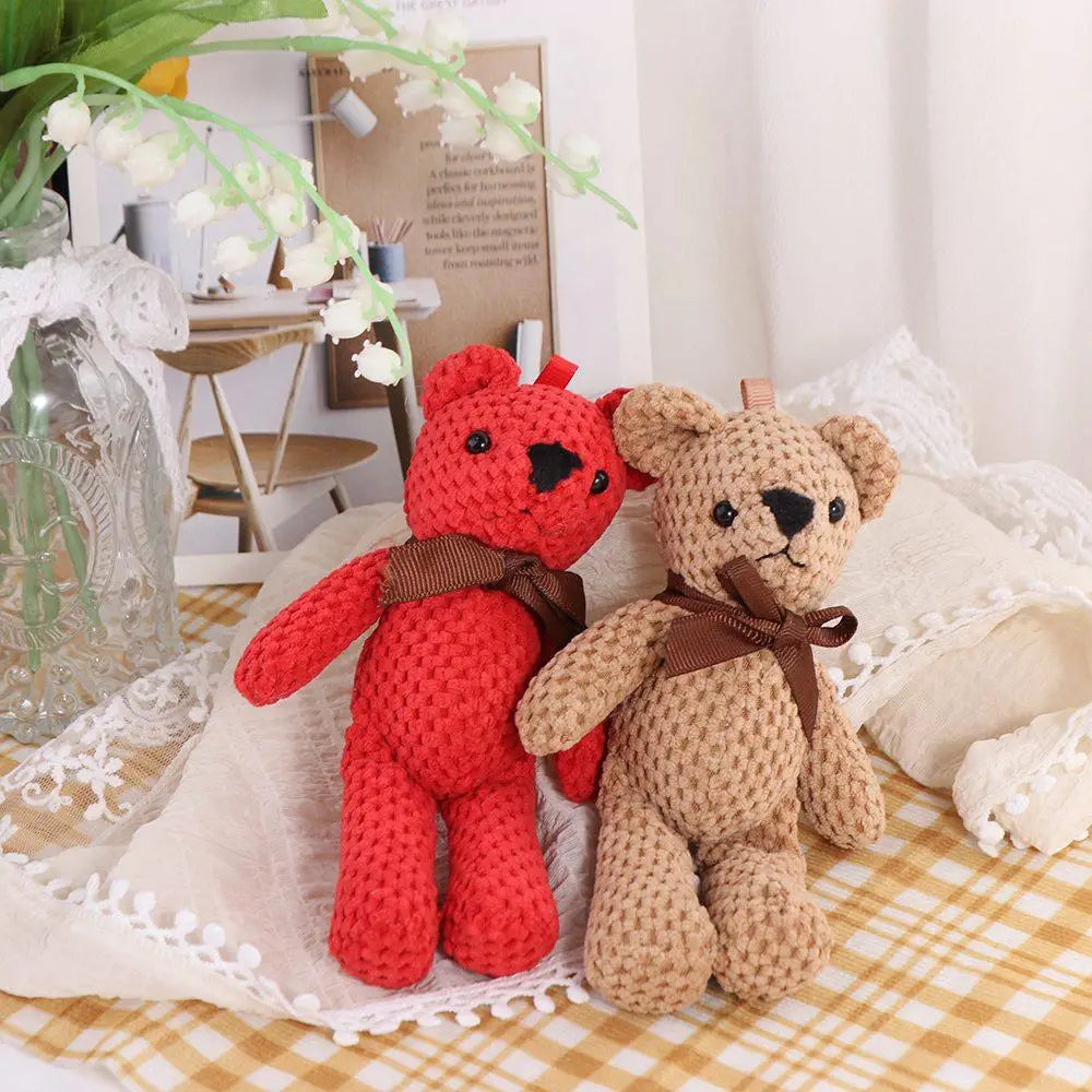 Deux peluches en forme d’ourson teddy au crochet faites à la main, aux couleurs rouges vives et beige doux, chacune confectionnée en matière tricotée au crochet et ornée d’un nœud de ruban marron autour du cou.