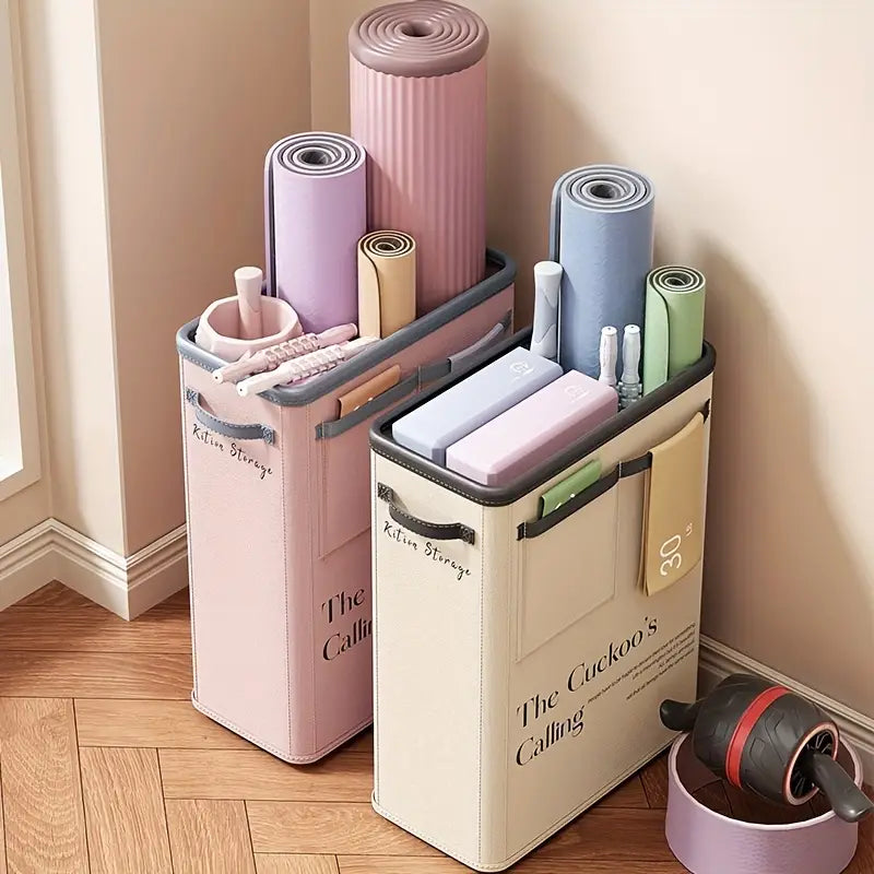 Pastel pink and cream fabric storage bins with gray trim labeled kition storage and the cuckoo’s calling holding rolled yoga mats and exercise equipment in a yoga mat storage basket fitness organizer.