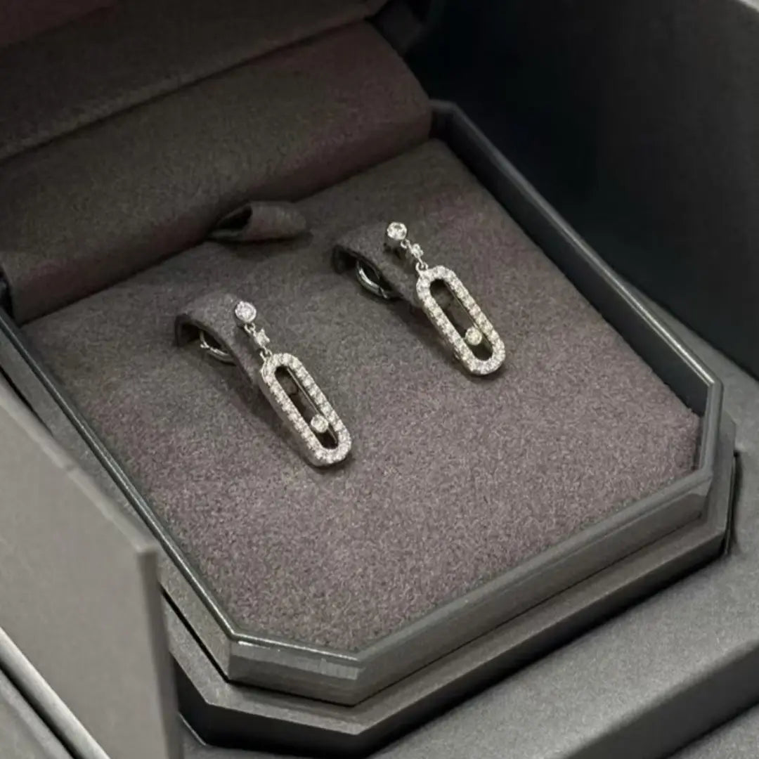 Une paire de boucles d’oreilles pendantes rectangulaires en argent et diamants, conçue comme des formes élégantes de trombones dans un ton argenté, rehaussées de diamants étincelants.