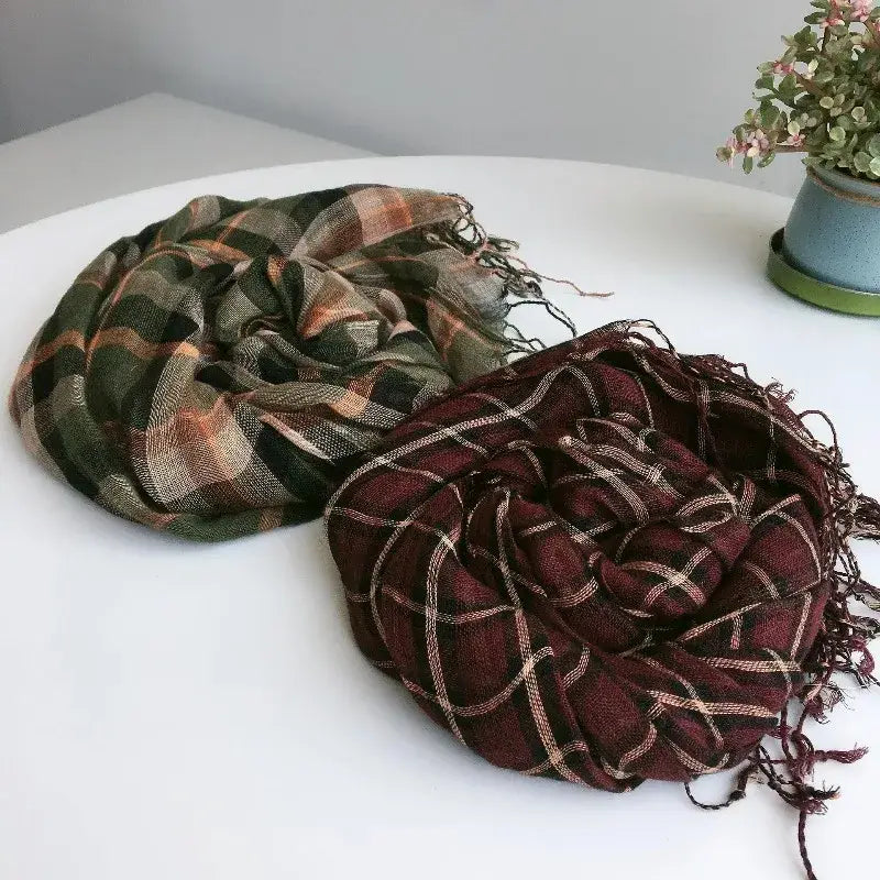 Dos bufandas para mujer de cuadros dobladas, con diseño tipo chal envolvente largo y tejido en punto ligero, en tonos oliva y óxido, con bordes deshilachados, y otra en burdeos oscuro con franjas color crema y flecos a juego.