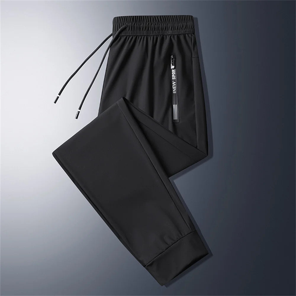 Jogger de hombre fitness 5XL en negro, con cintura ajustable mediante cordón y un bolsillo vertical con cremallera con nueva imagen de marca deportiva para uso atlético.