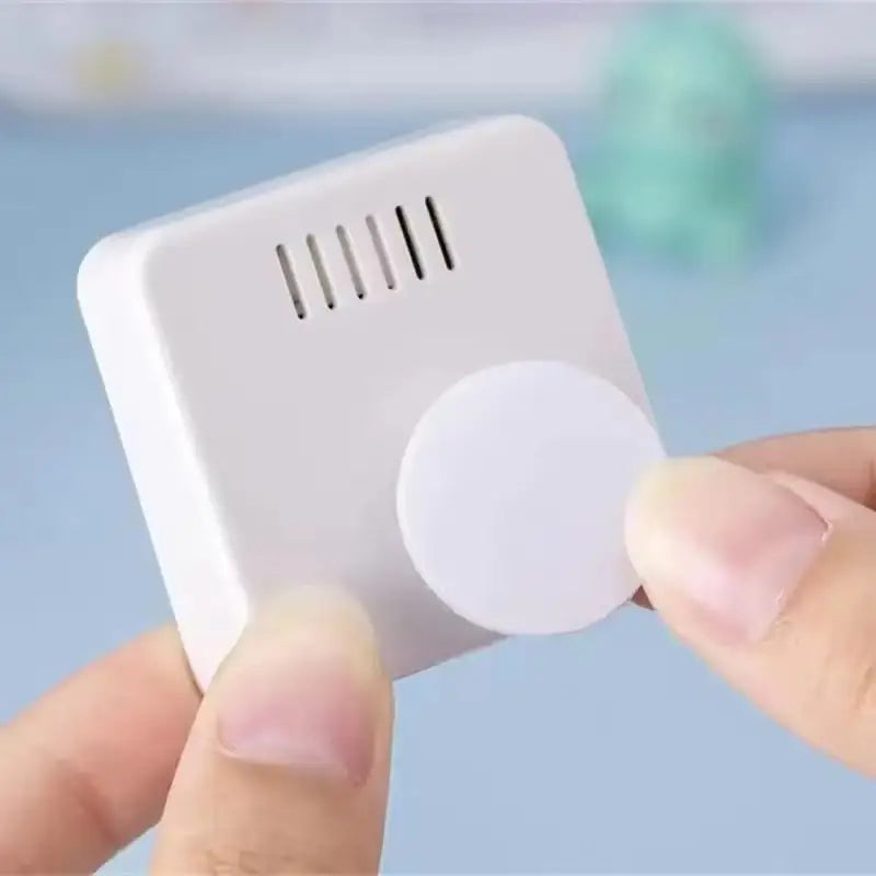 white rectangular smoke detector with circular adhesive pad and vertical ventilation slits designed as part of a digital weather desktop alarm clock