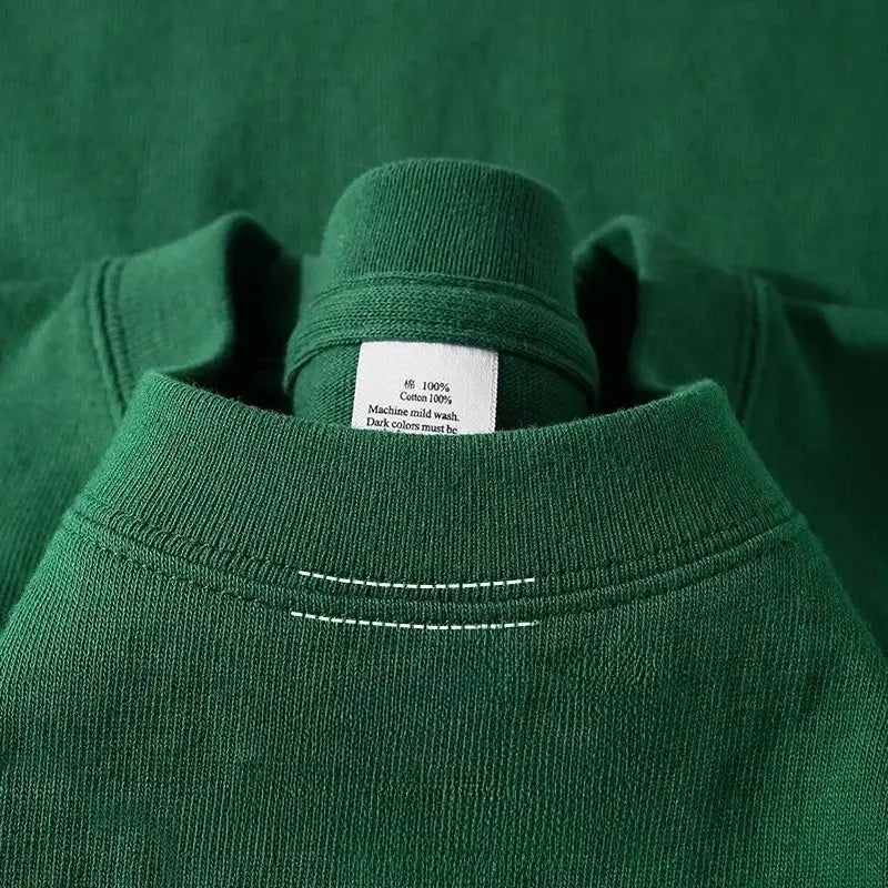 Sudadera de algodón verde oscuro de cuello tipo tripulante, con costuras blancas a lo largo de la zona del cuello, combinada con una camiseta de algodón de cuello redondo color azul marino