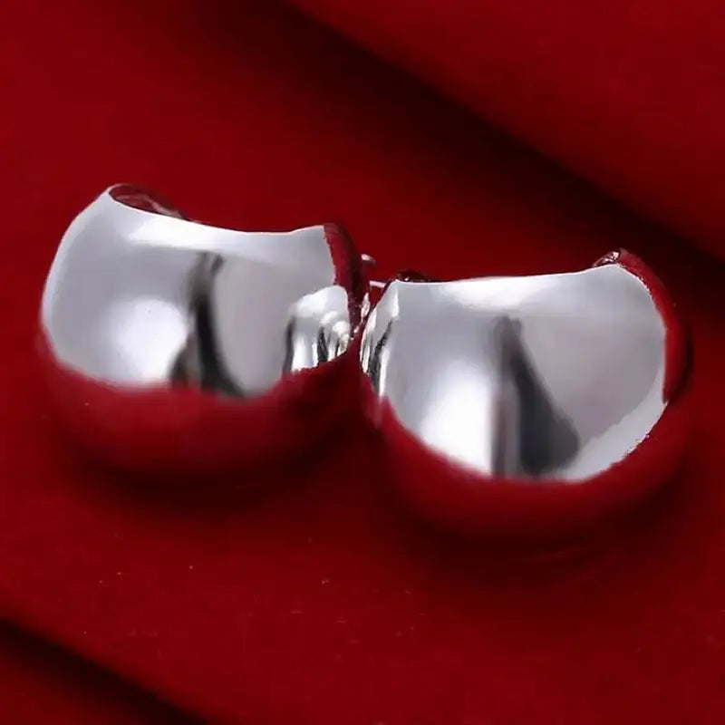 Boucles d’oreilles créoles minimalistes en argent sterling 925, avec une surface lisse et réfléchissante argentée brillante et une conception légèrement courbée.