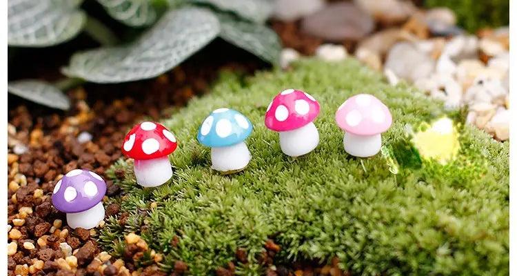 Des figurines miniatures en résine de champignon colorées, avec des chapeaux peints brillants et des tiges blanches, disposées sur de la mousse verte, pour la décoration d’un jardin féerique.