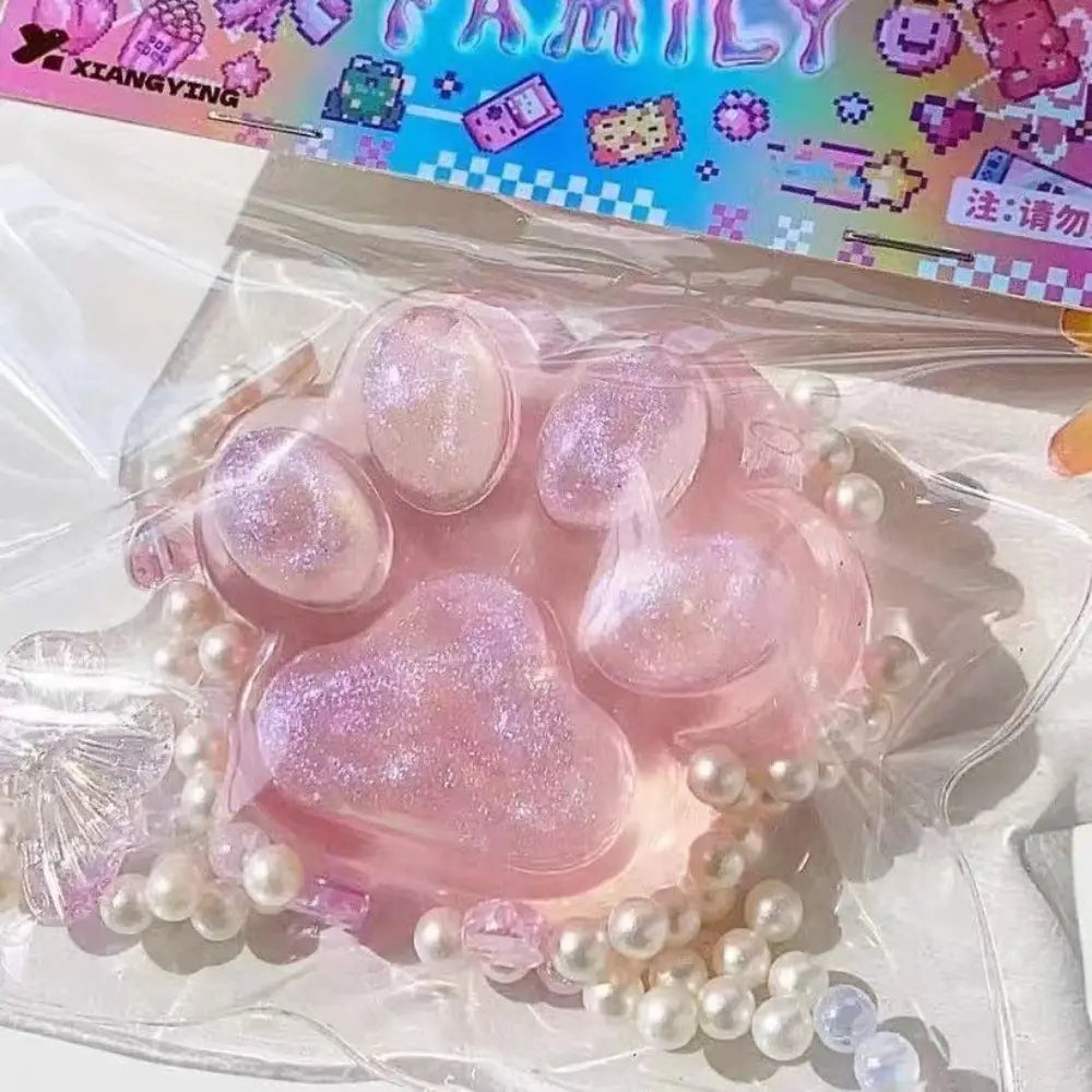juguete exprimible de resina con purpurina rosa y forma de pata de gato, con silicona de liberación lenta y gradual, rodeado de perlas blancas para aliviar el estrés