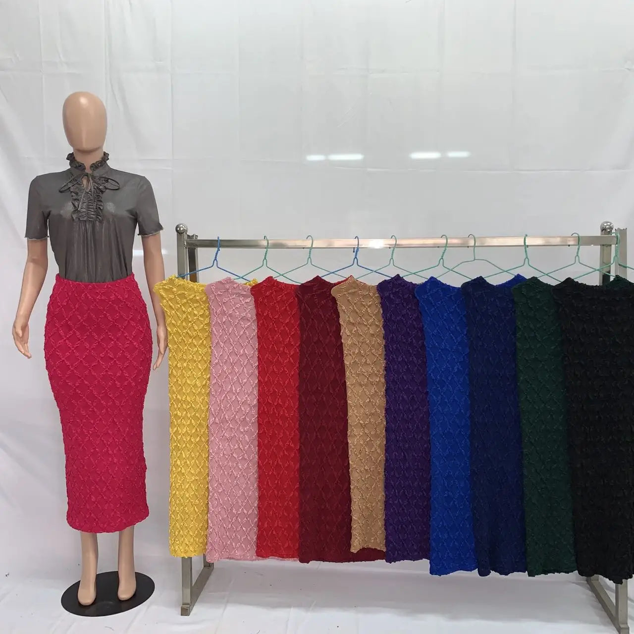 A vibrant red high waist knit midi skirt with a slim fit and textured fabric displayed on a mannequin alongside various colored skirts.