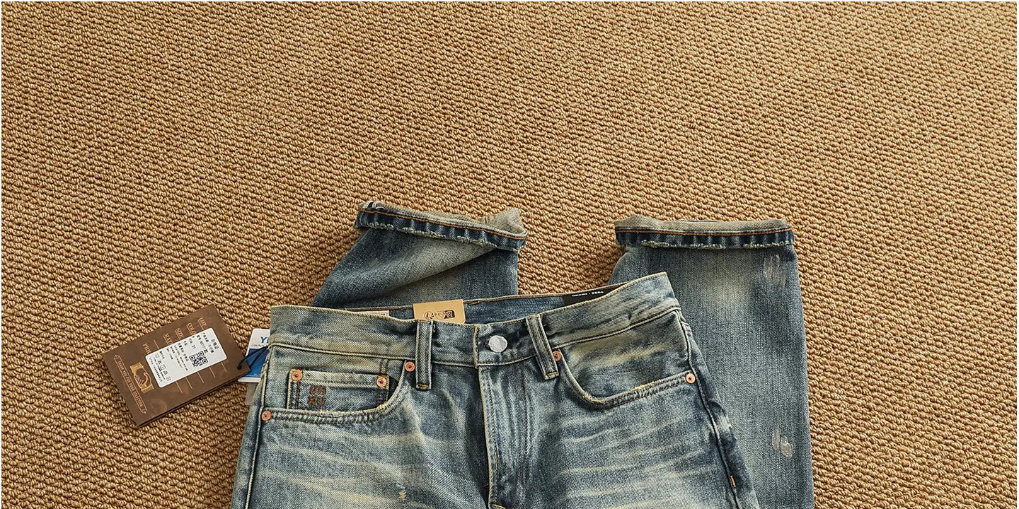 A pair of distressed patchwork denim jeans for men in faded blue with a worn-in look and copper-colored hardware.