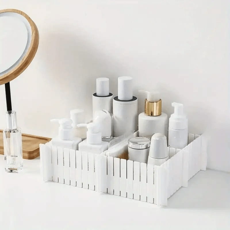 Adjustable white plastic drawer divider partition with a picket fence design organizing various skincare and beauty bottles.