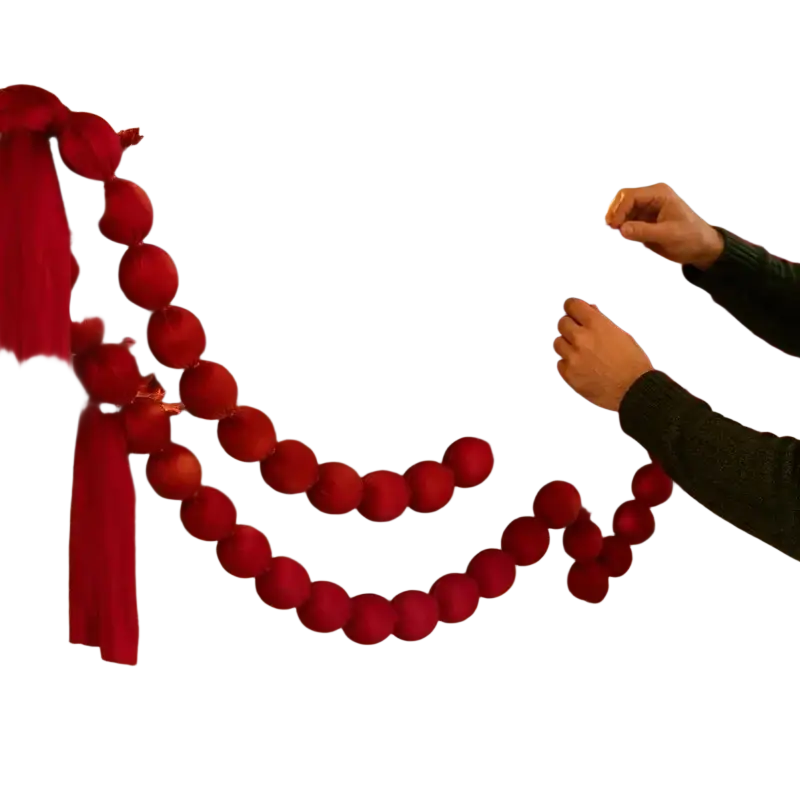 Burgundy velvet ball garland draped over a stone fireplace mantel as a soft fabric ornament for holiday decoration